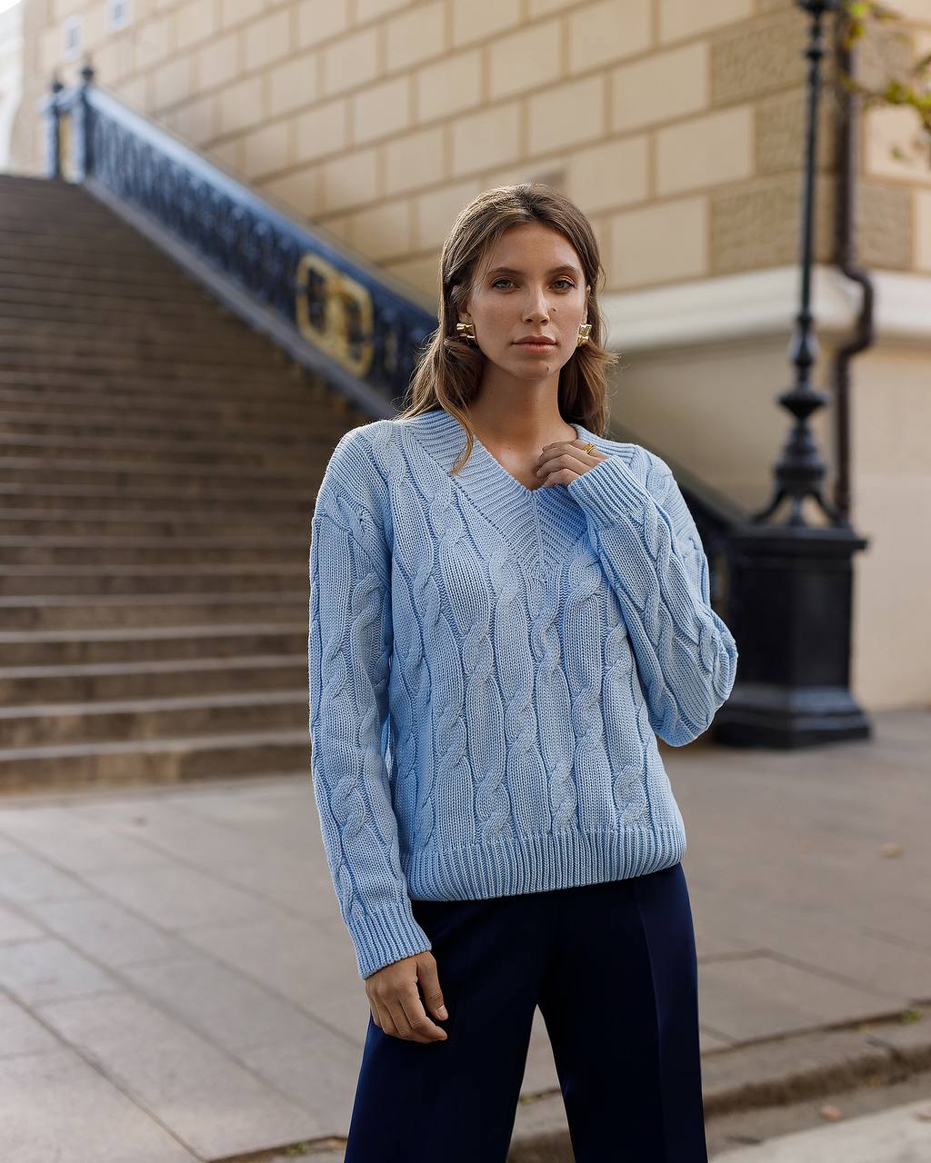 Woman wearing a light blue cable knit sweater standing outdoors on a city street.