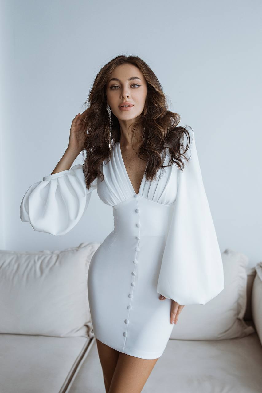 Woman wearing a white dress with bell sleeves in a minimalistic setting