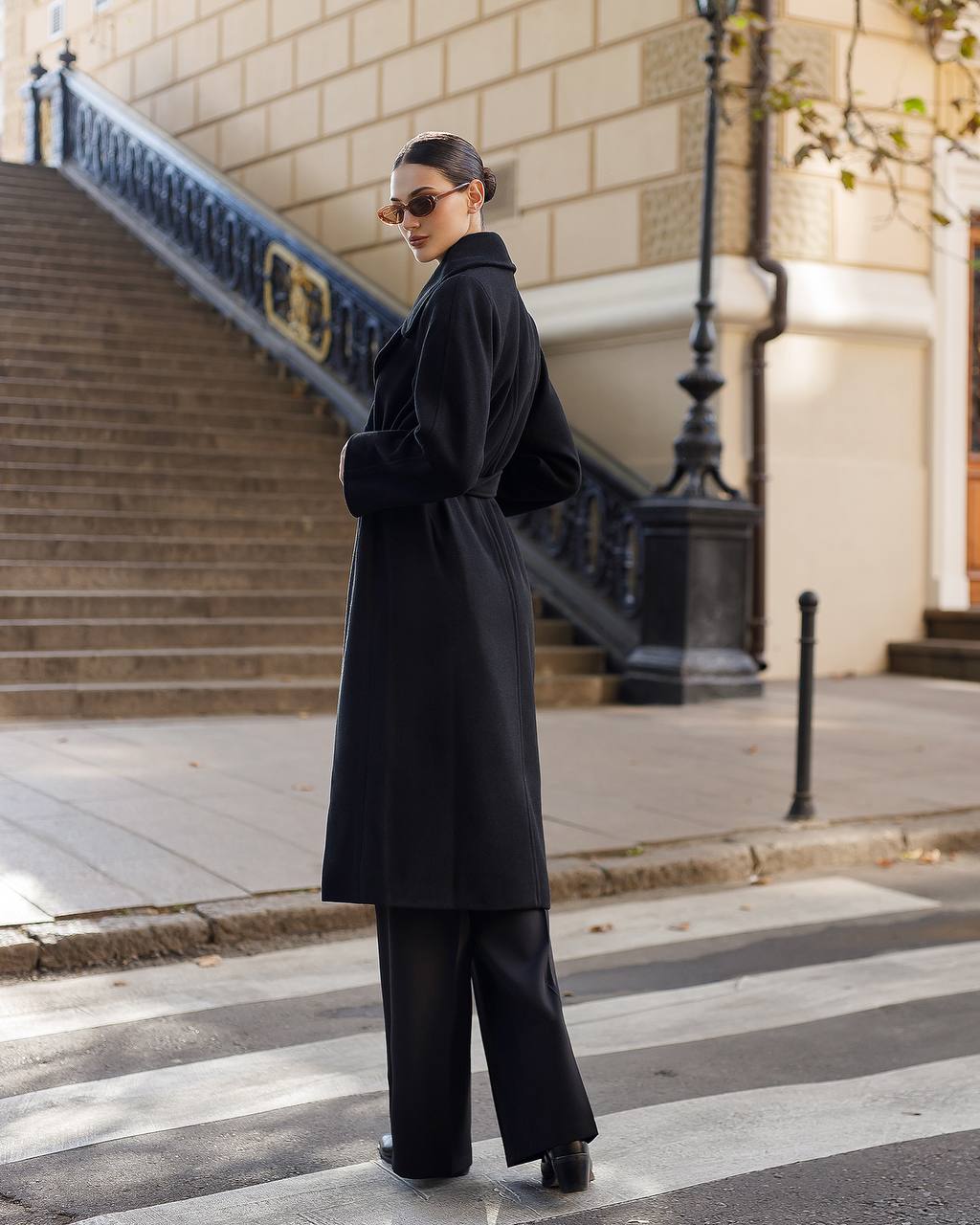 Person wearing a black coat and pants walking on a city street.