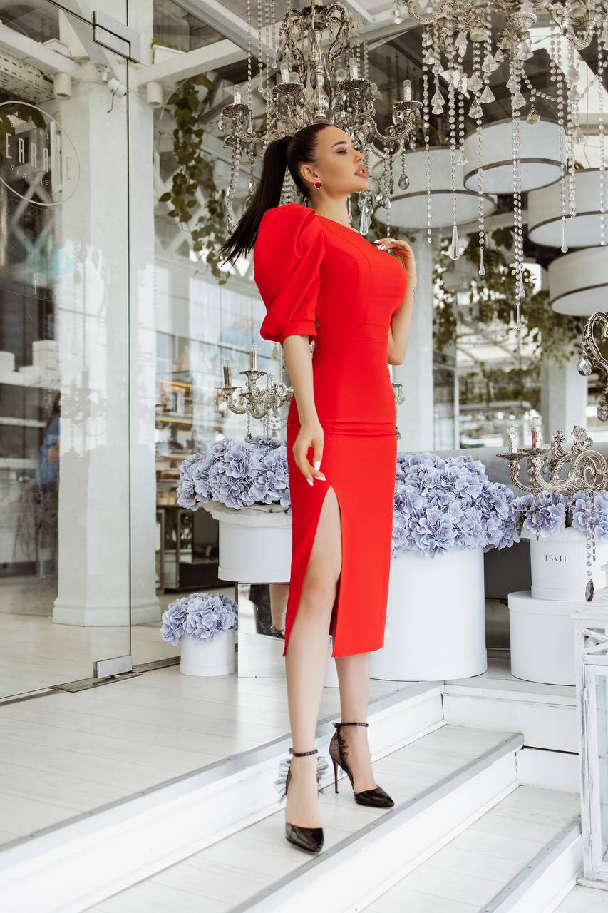 Woman in a red dress standing in a stylish interior setting with chandeliers and floral arrangements.