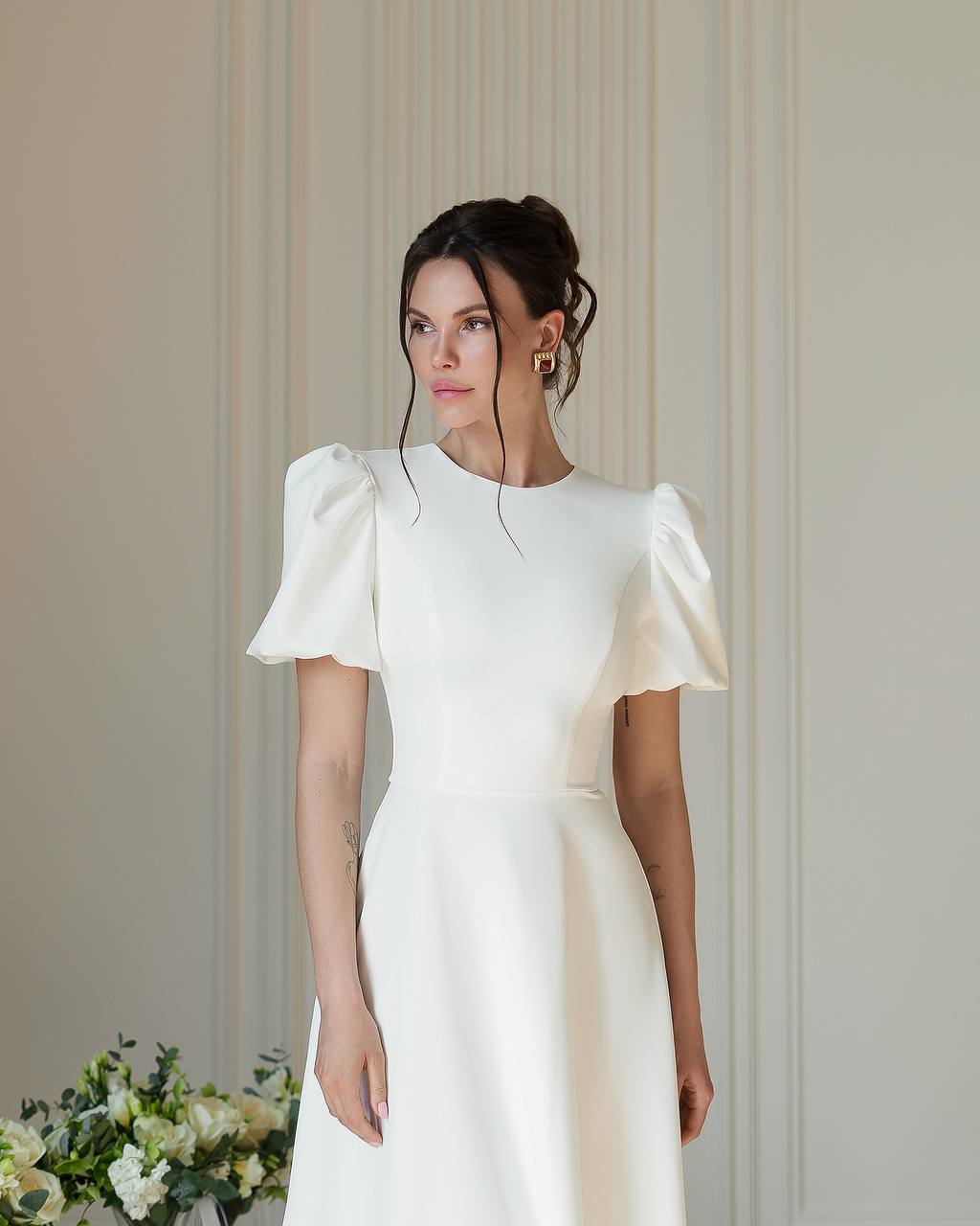 Woman wearing a white dress with puffed sleeves against a neutral background