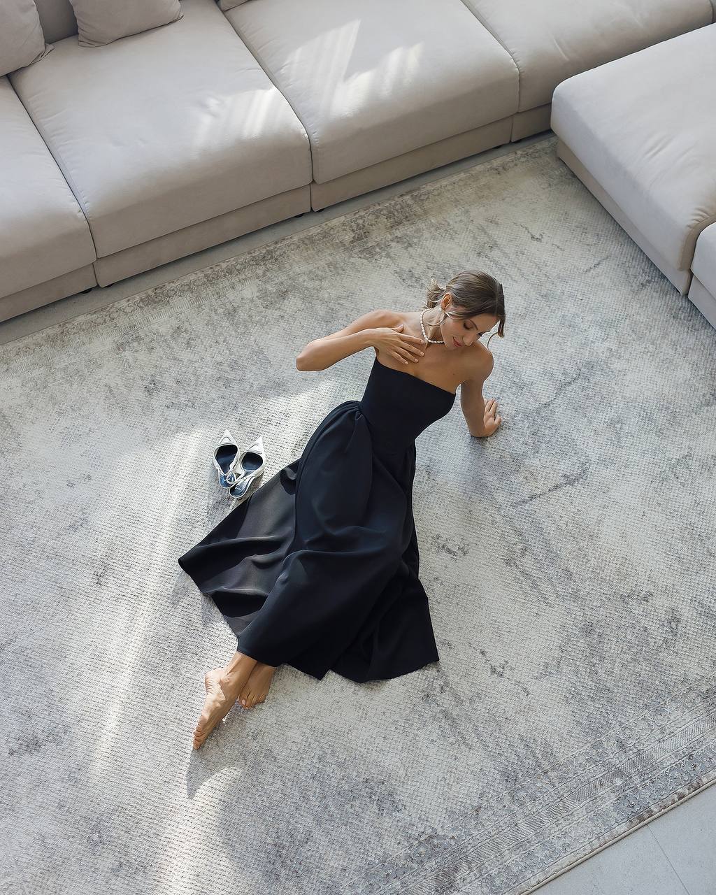 Woman in a black dress sitting on a textured rug in a modern living room.