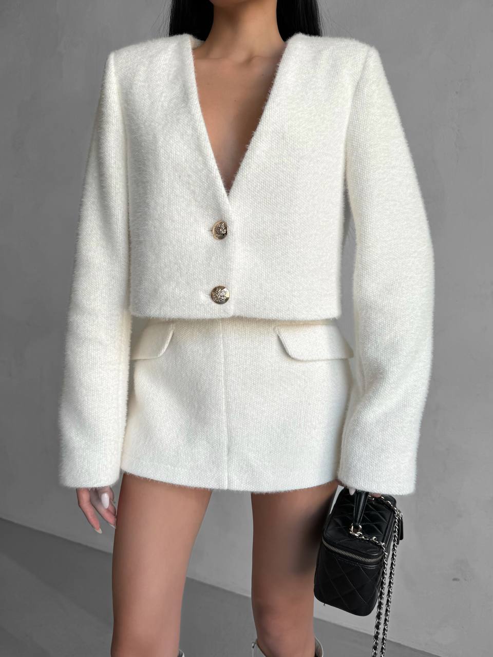 White textured blazer and skirt set with a black handbag on a gray background