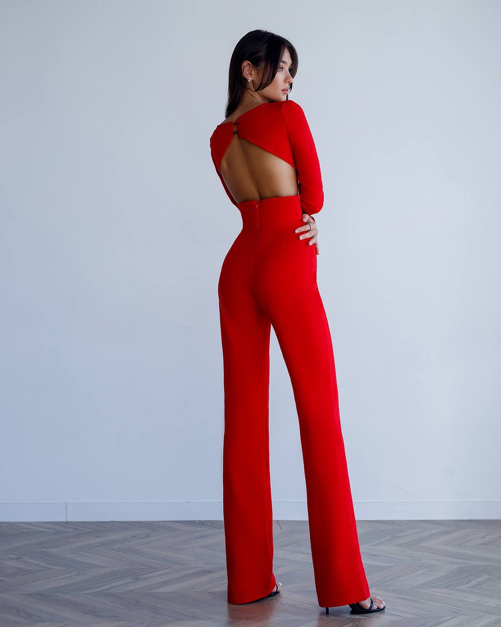 Woman wearing a red jumpsuit with cut-out design on a plain background