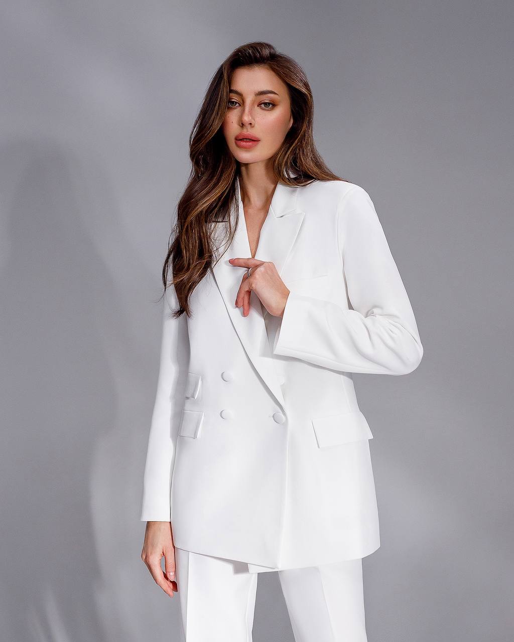 Woman wearing a white suit against a gray background