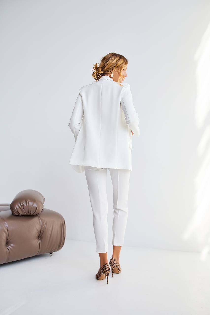 Woman in a white outfit standing in a minimalistic room with a brown leather chair.