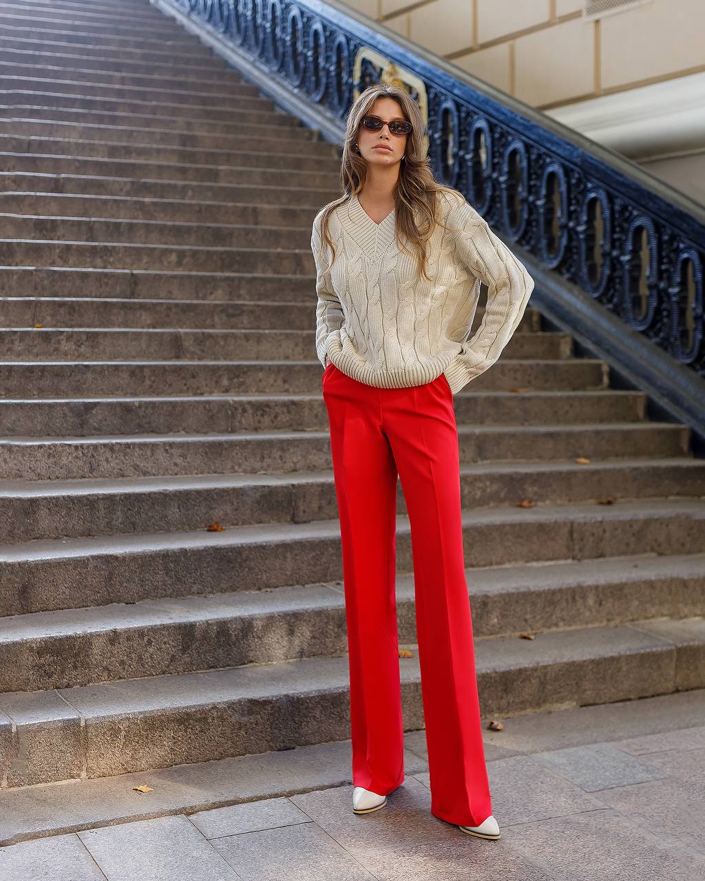 Woman in a cream sweater and red pants standing on stone steps with decorative balustrade.