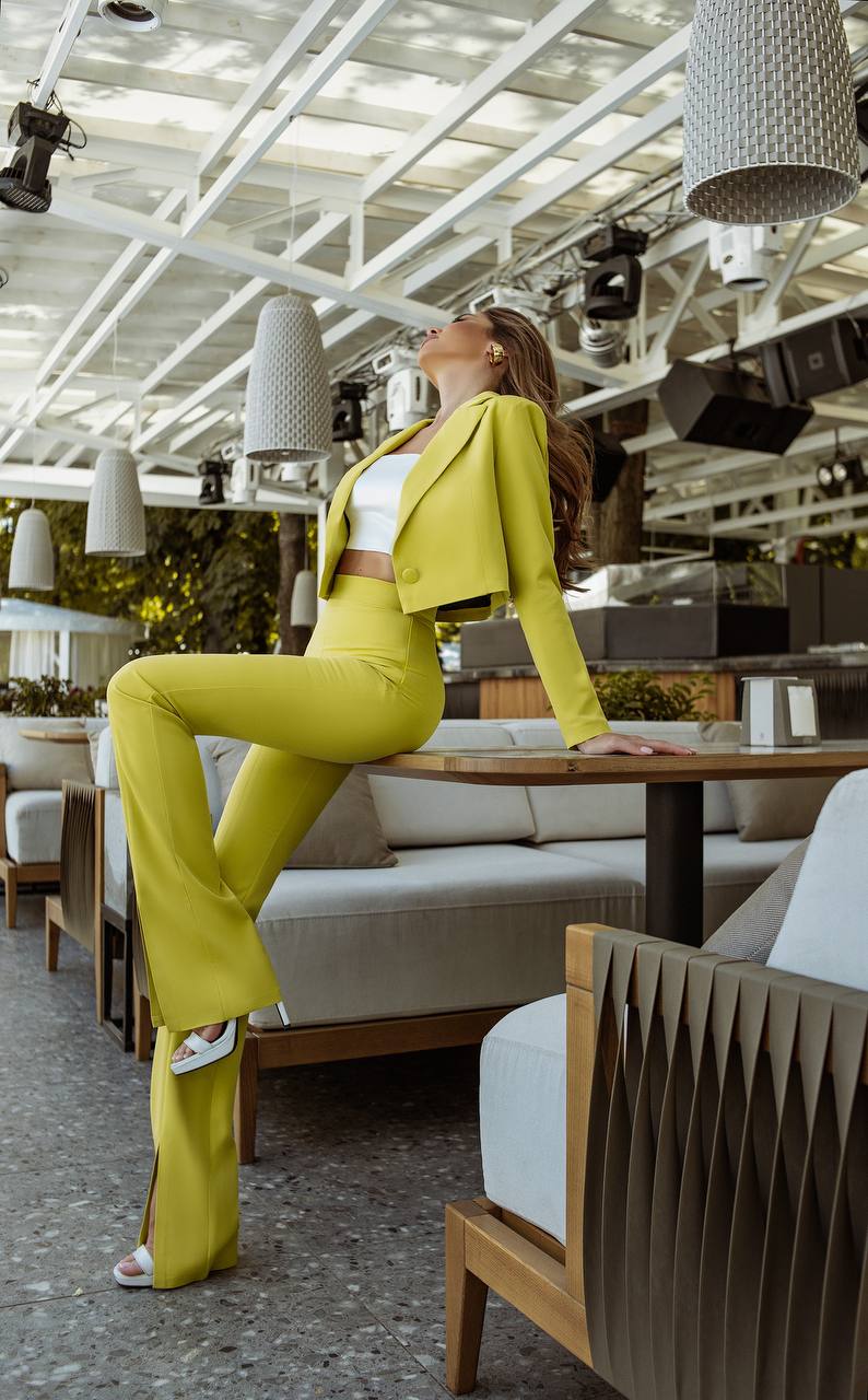 Woman in a bright yellow suit standing in a modern indoor setting with tables and chairs.