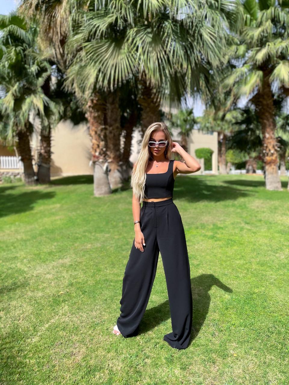 Woman in black outfit standing on grass with palm trees in the background