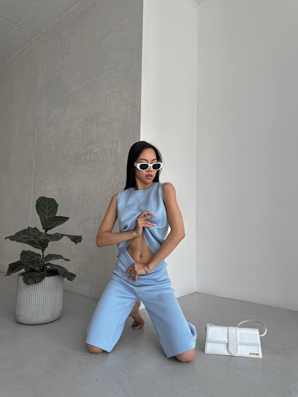 Person wearing a light blue sleeveless top and wide-leg pants in a minimalistic room.
