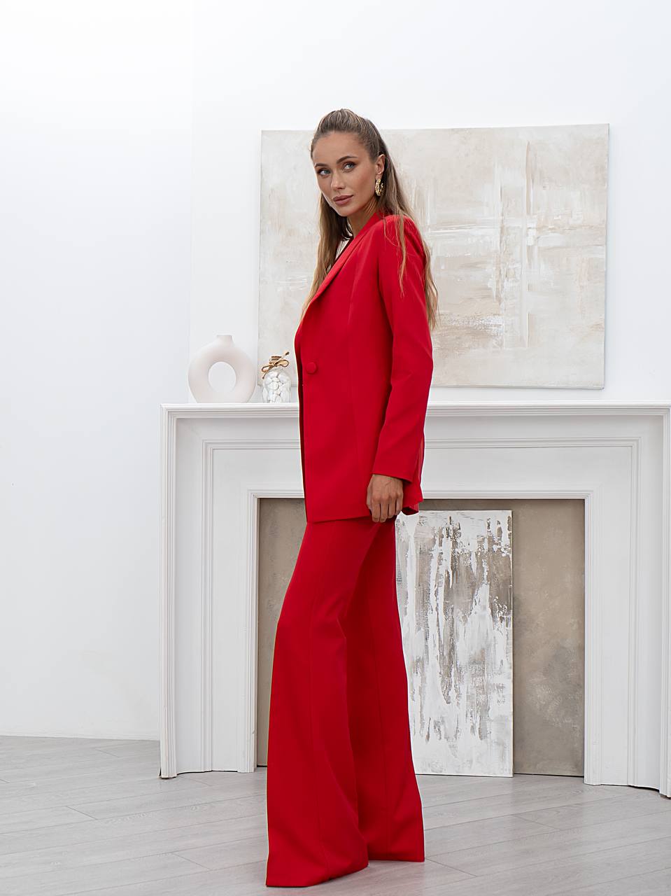 Woman in a red suit standing in a room with white walls and a fireplace.