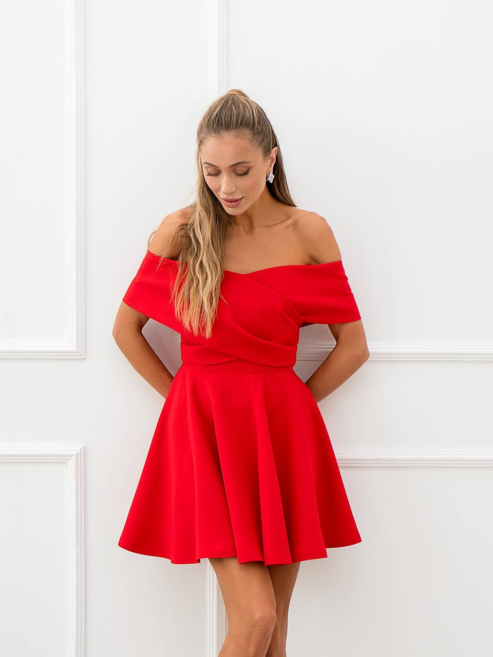 Woman wearing a red off-shoulder dress against a white wall