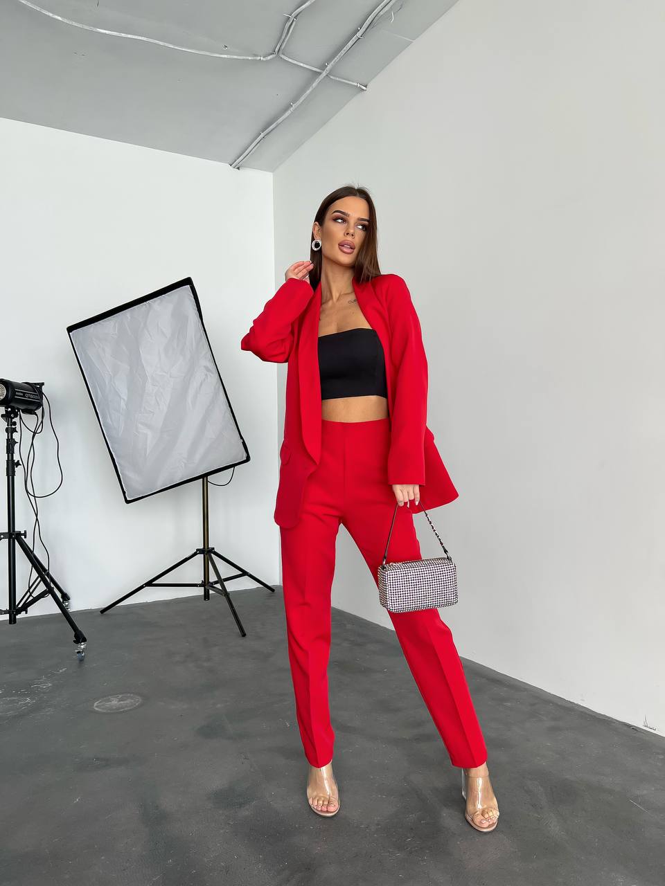 Woman in a red suit standing in a studio setting with photography equipment.