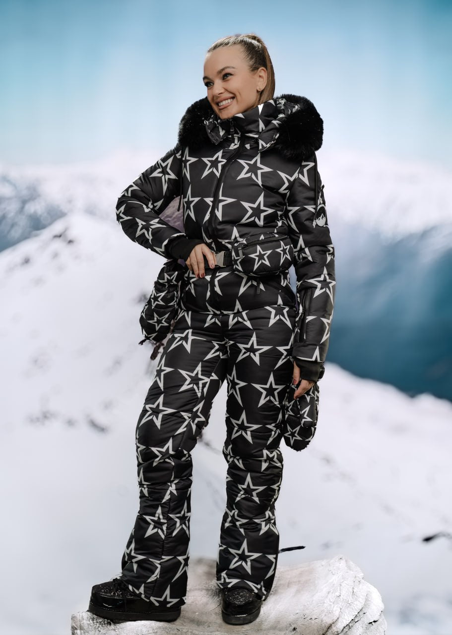Person wearing a black snowsuit with white star patterns standing on a snowy mountain.