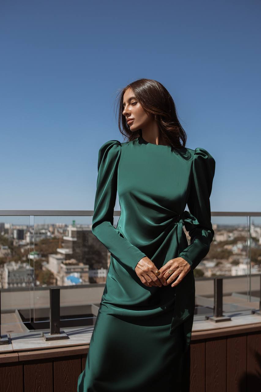 Woman in a green dress standing on a rooftop with a cityscape in the background