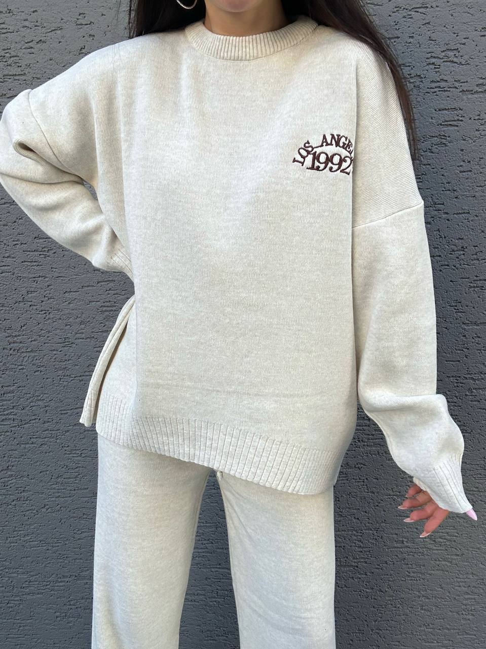 Person wearing a cream-colored sweater with text on it against a gray background