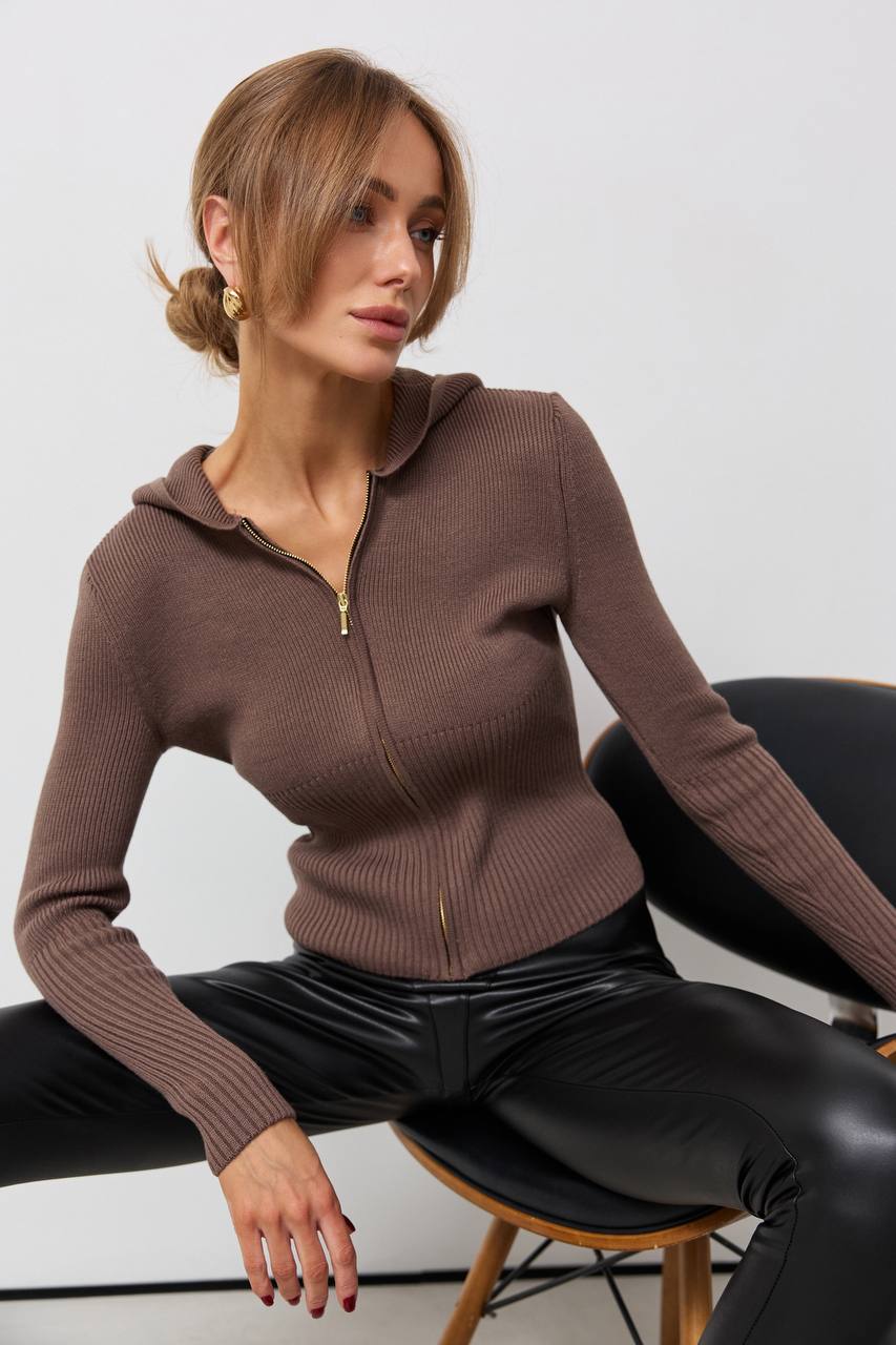 Woman wearing a brown zip-up sweater sitting on a chair against a white background