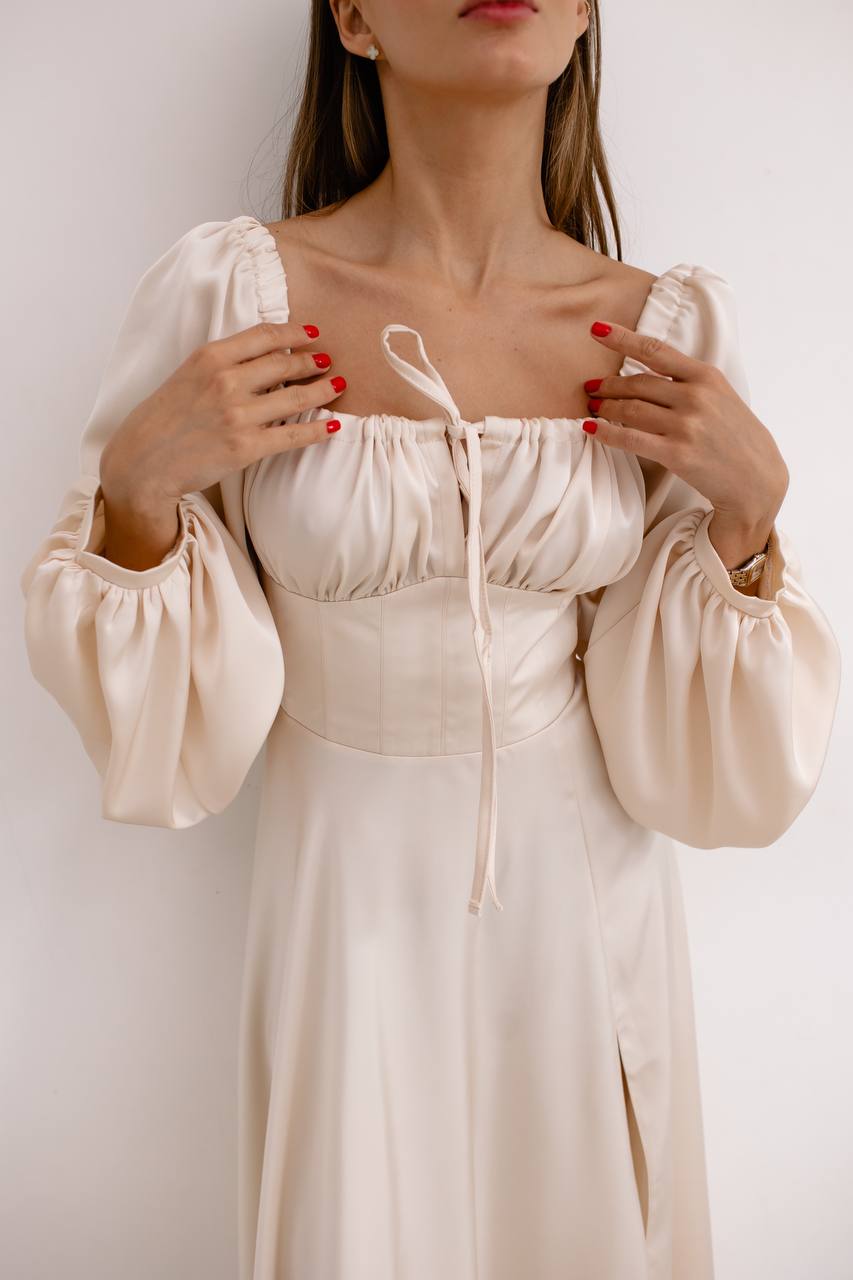 Woman wearing a beige dress with long sleeves against a white background