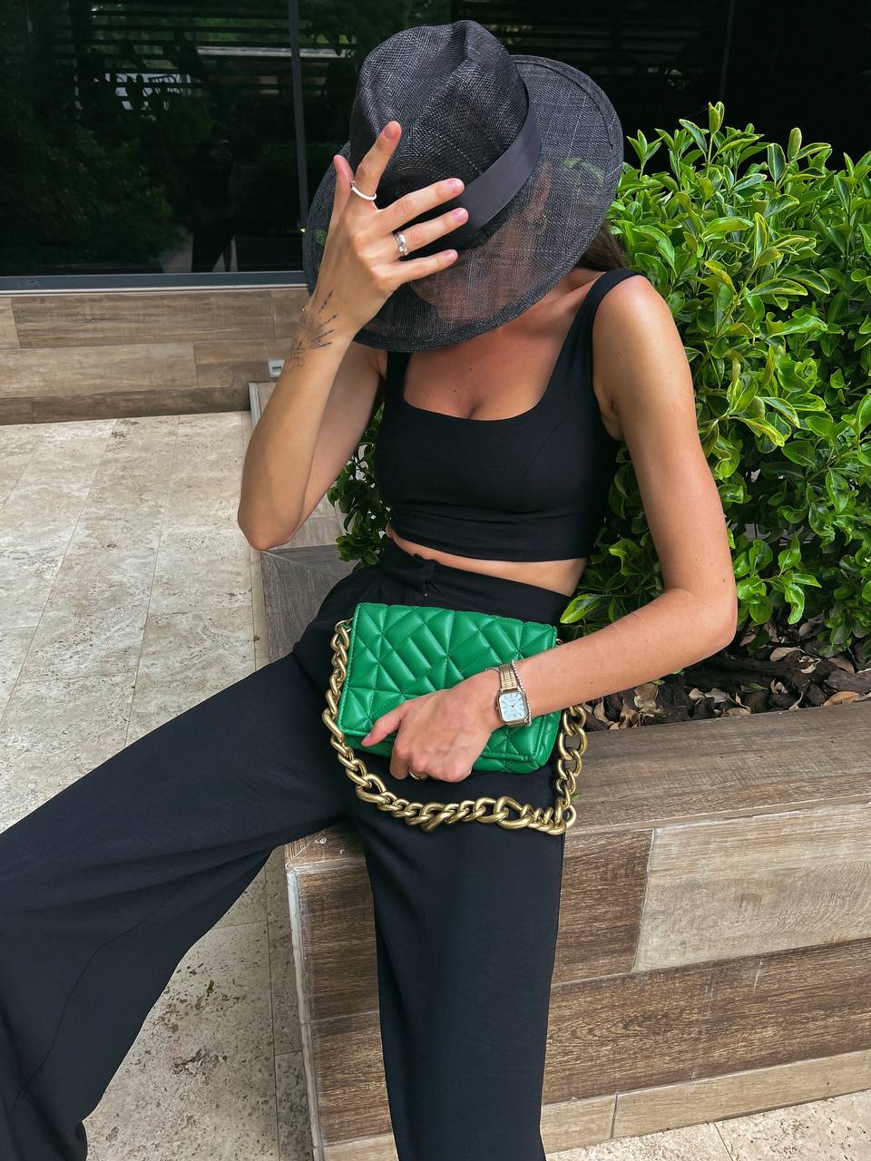 Person wearing a black outfit with a green quilted handbag, standing outdoors.
