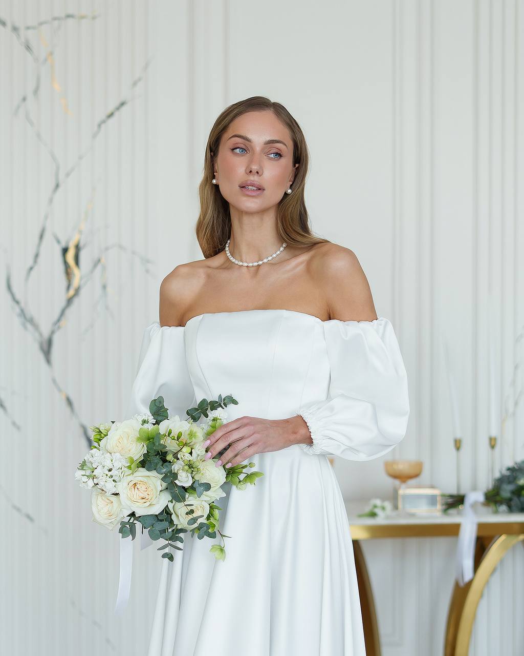 Woman in a white wedding dress holding a bouquet in an elegant indoor setting.