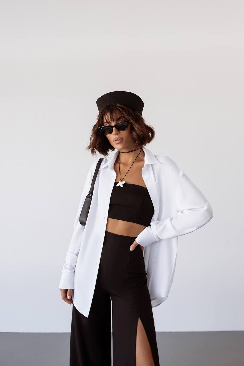 Person wearing a black outfit with a white shirt over it, standing against a plain background.