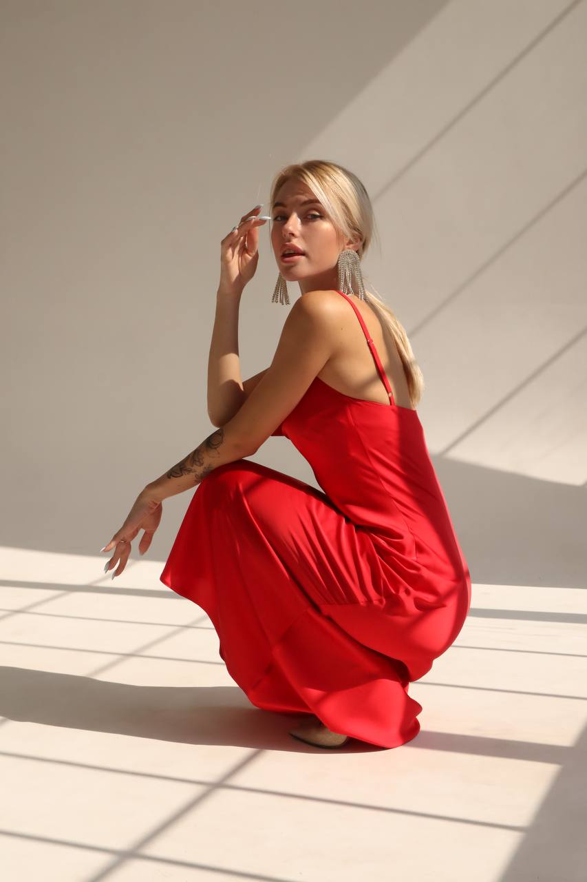 Woman in a red dress sitting on a white floor with sunlight casting shadows.