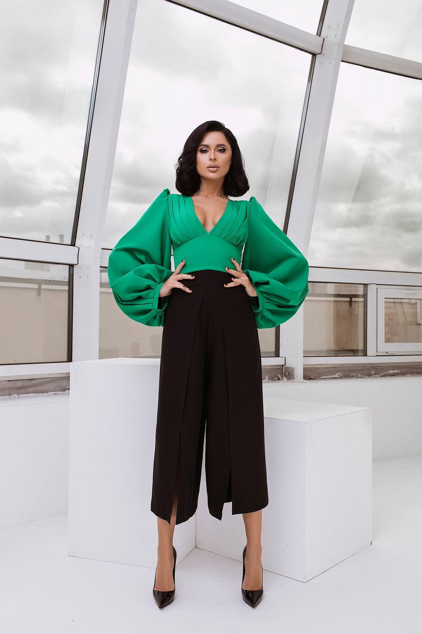 Woman wearing a green blouse and black pants in a modern indoor setting