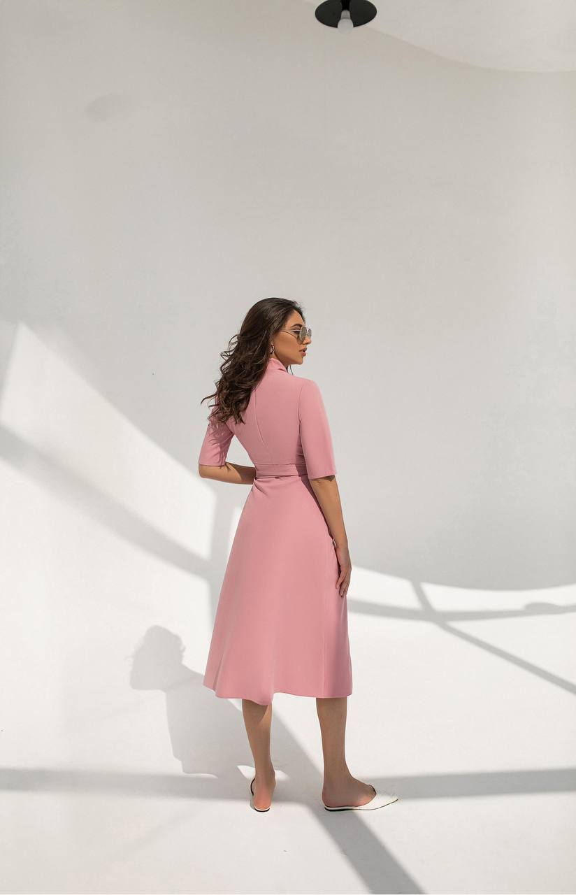 Woman wearing a pink dress standing in a well-lit room with white walls.