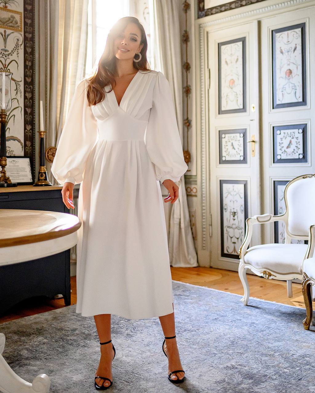 Woman in a white dress standing in an elegant room with decorative elements.