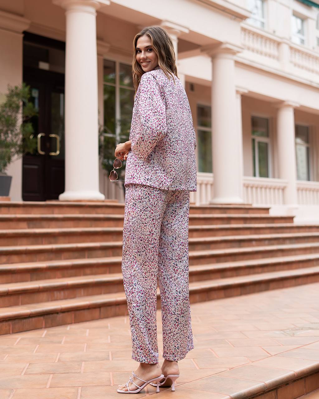 Woman in a floral outfit standing on steps in front of a building with columns.