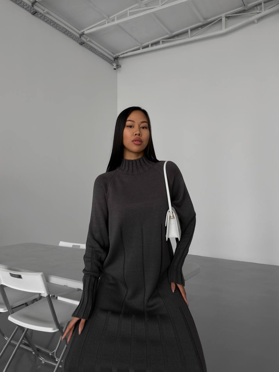Woman wearing a black outfit with a white bag in a minimalistic setting