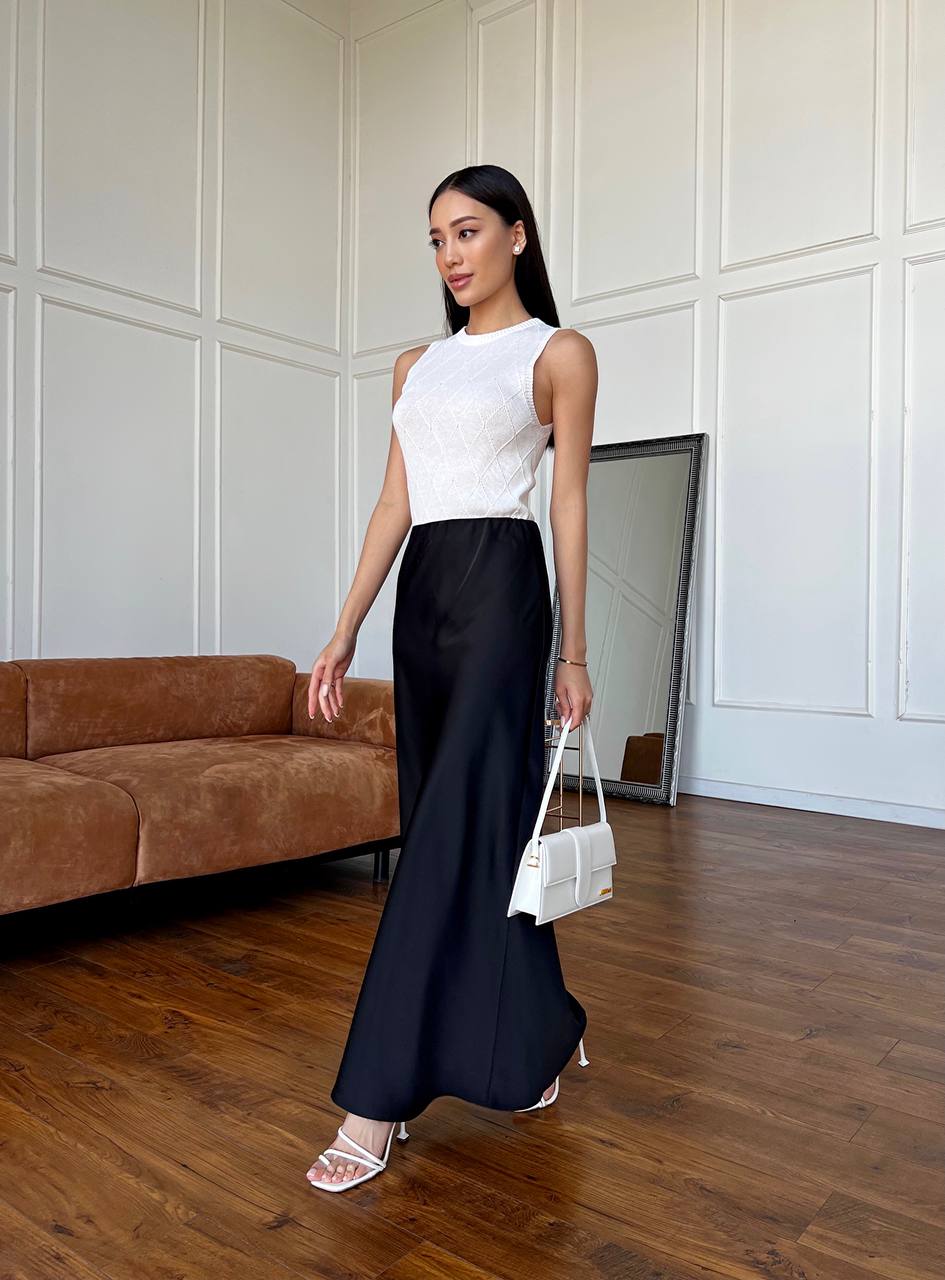 Woman in a white top and black skirt standing in a room with wooden flooring and a brown sofa.