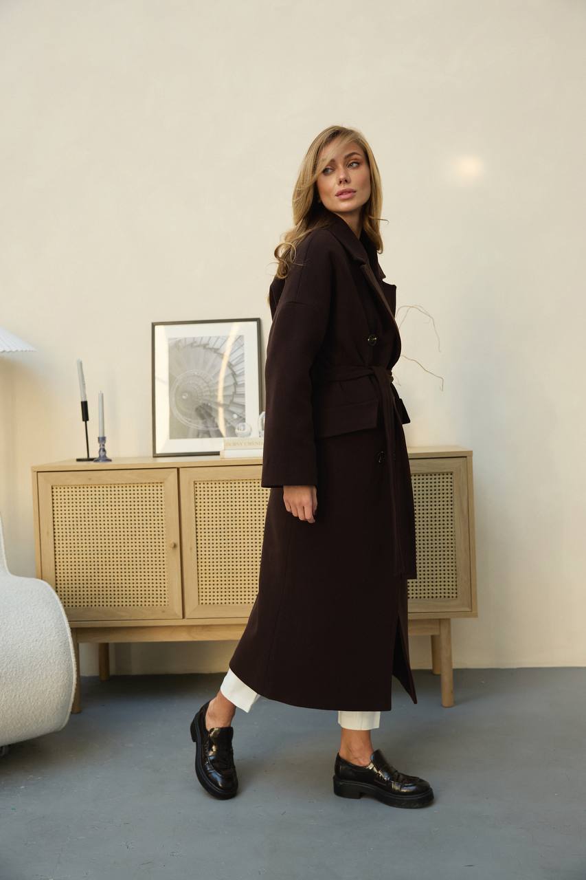 Woman wearing a long dark coat in an indoor setting with a neutral background