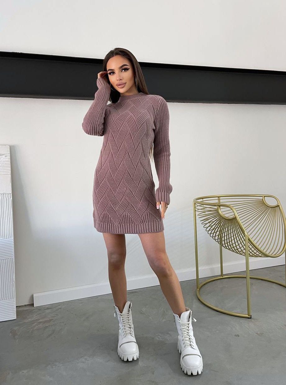 Woman wearing a ribbed knit dress and white boots in a minimalistic room.