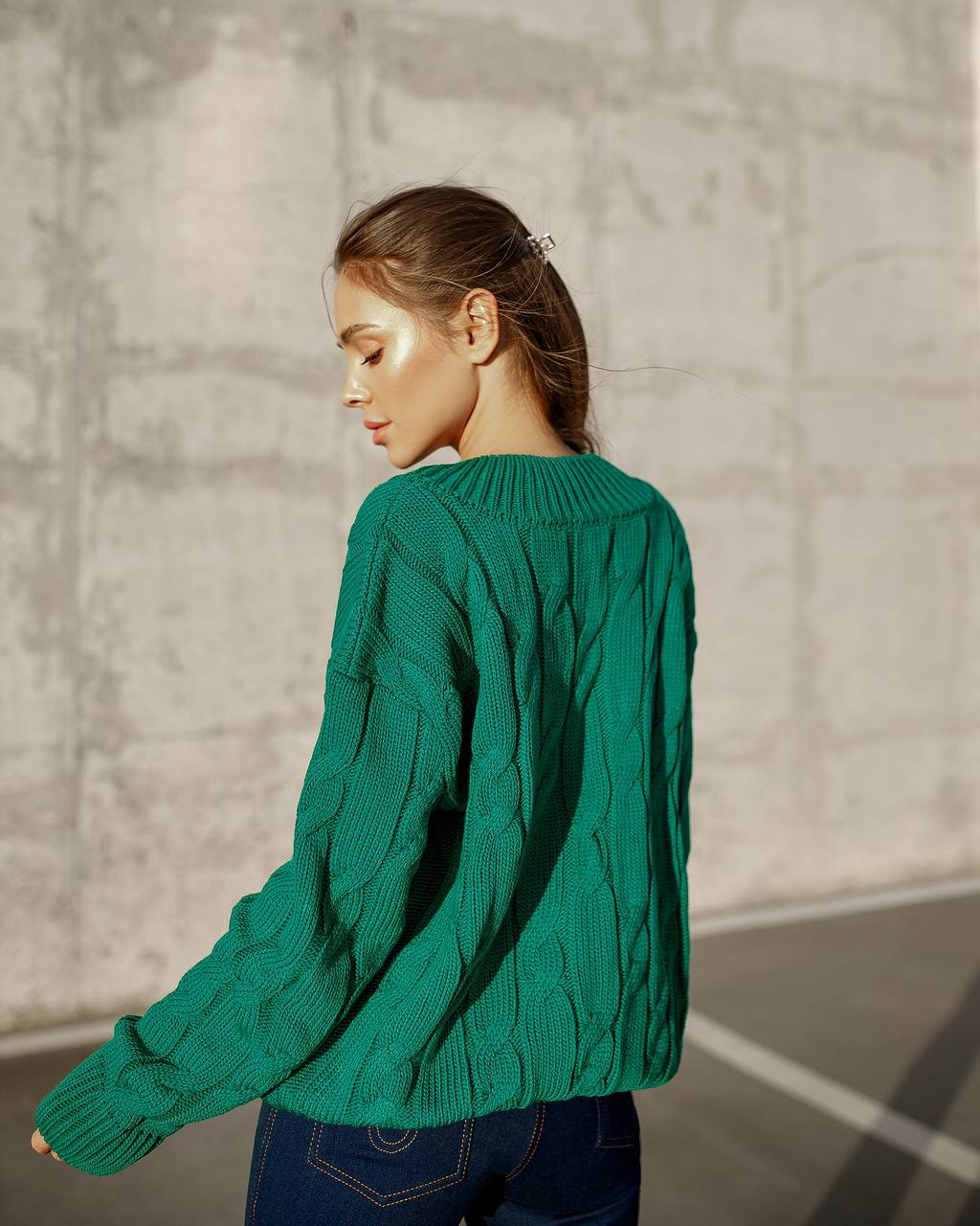 Woman wearing a green sweater against a textured wall.