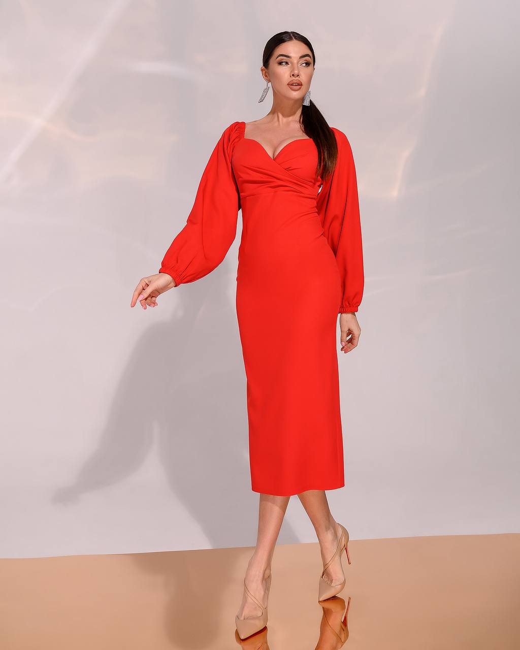 Woman wearing a red dress with long sleeves on a plain background