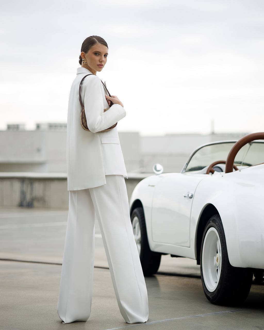 Woman in a white suit standing next to a vintage car