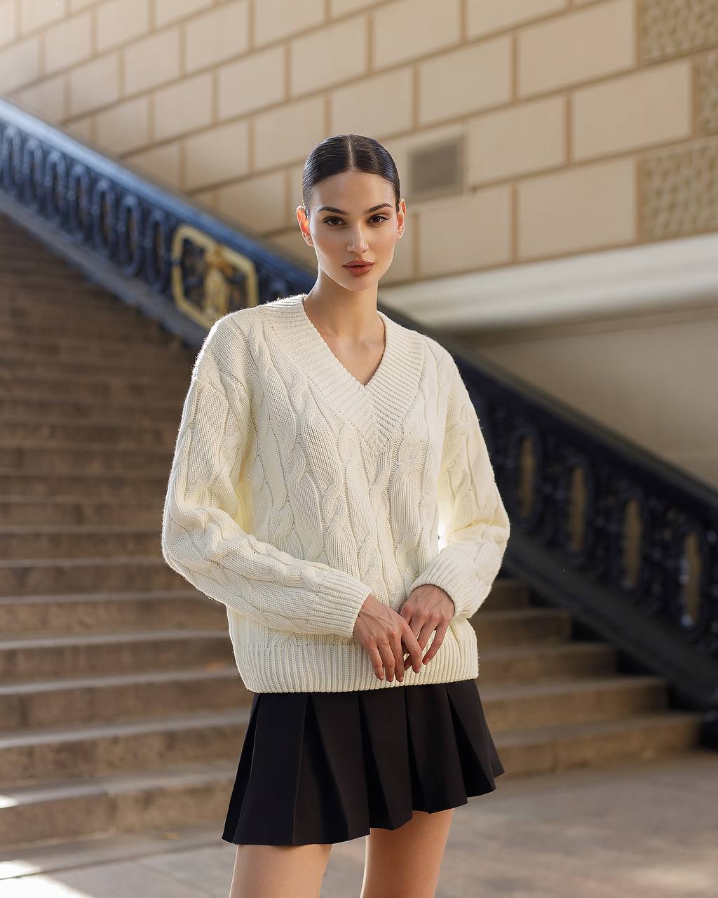 Woman wearing a cream sweater and black skirt standing on steps with a building in the background