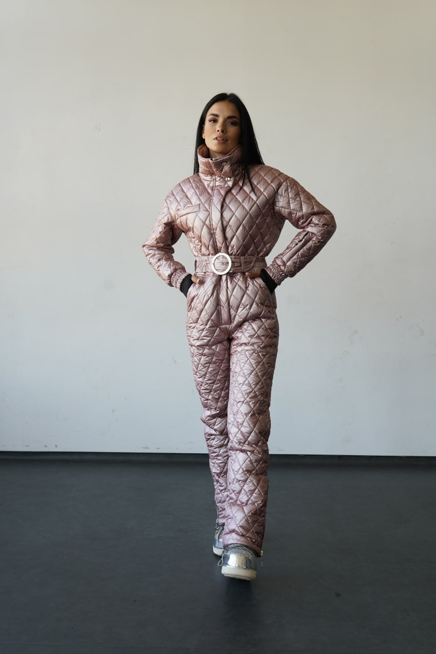 Person wearing a pink quilted jumpsuit with a belt against a plain background
