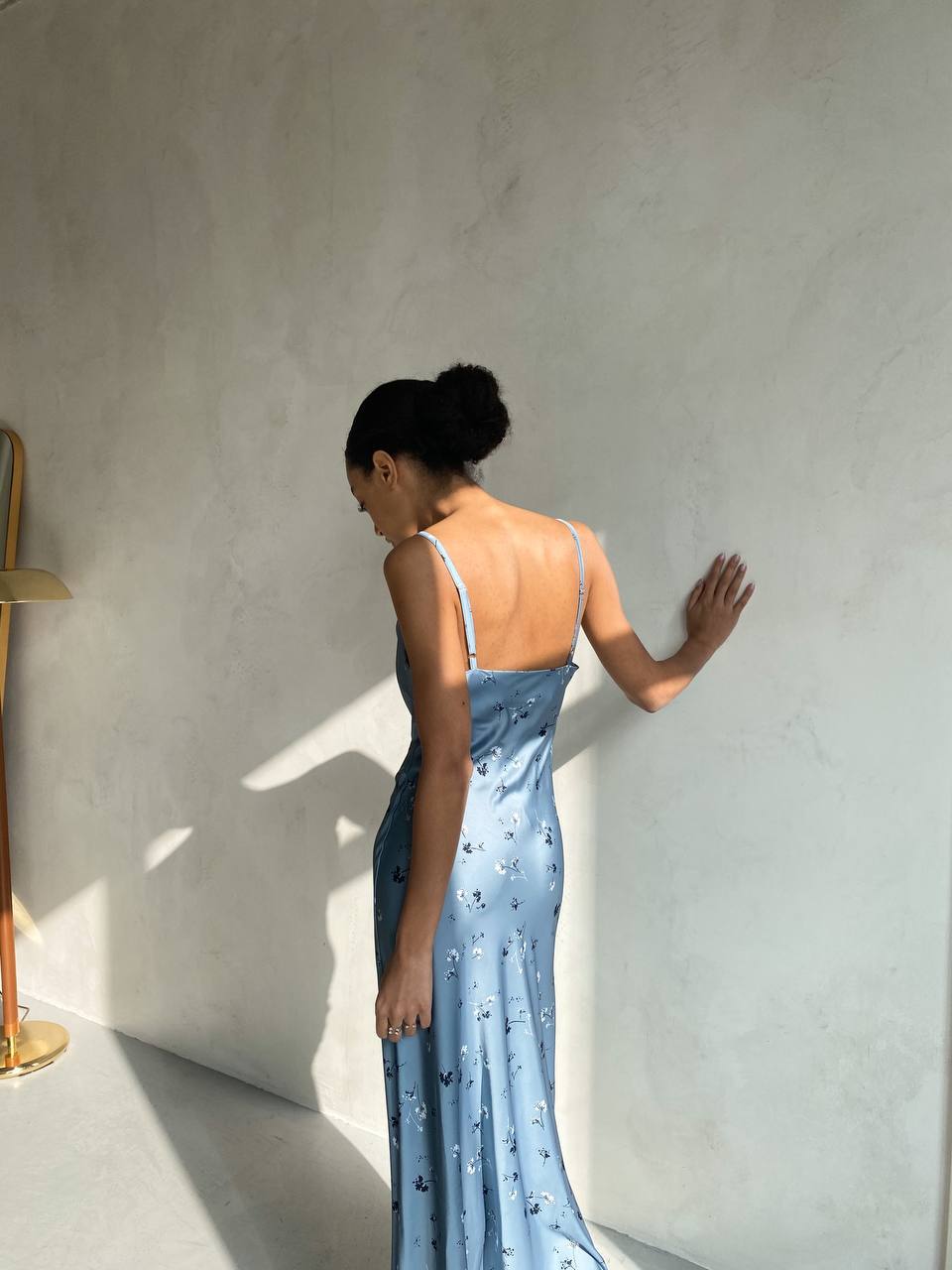 Woman in a blue floral dress standing against a light gray wall.