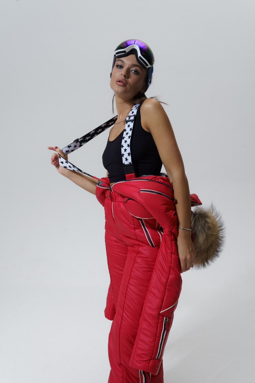 Person wearing a black top and red ski pants with goggles on a plain background