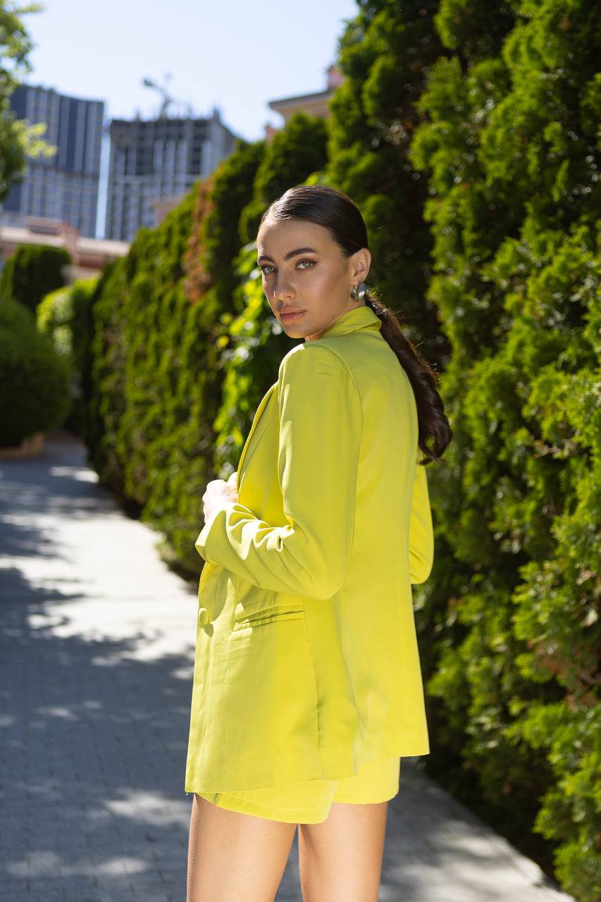 Woman in a bright yellow outfit standing outdoors with greenery and buildings in the background