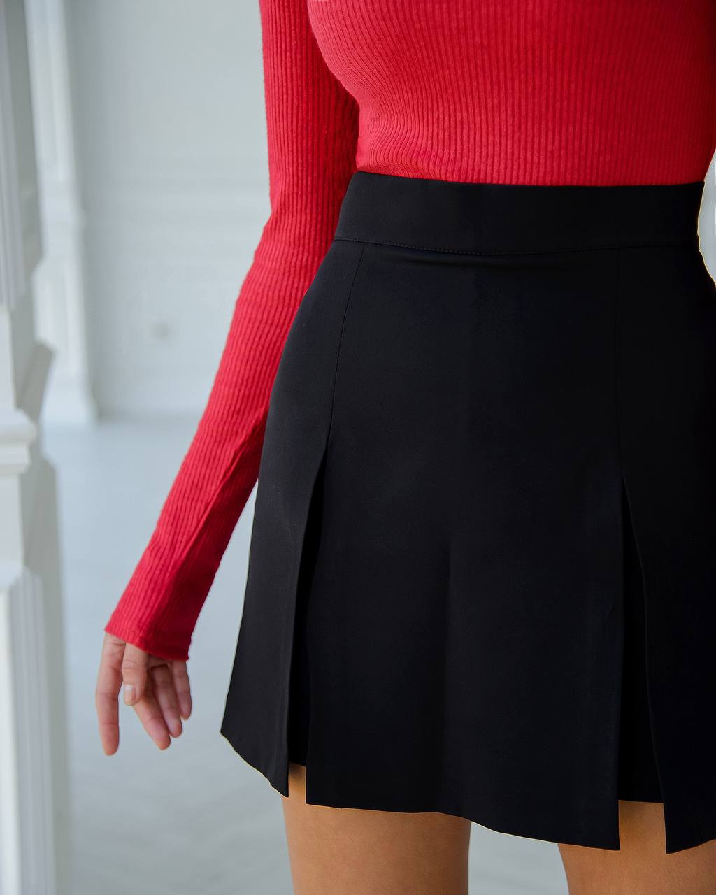 Person wearing a red long-sleeve top and black skirt against a white background