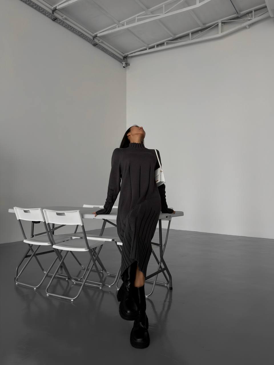 Person in a black outfit standing in an empty room with white walls and gray floor.