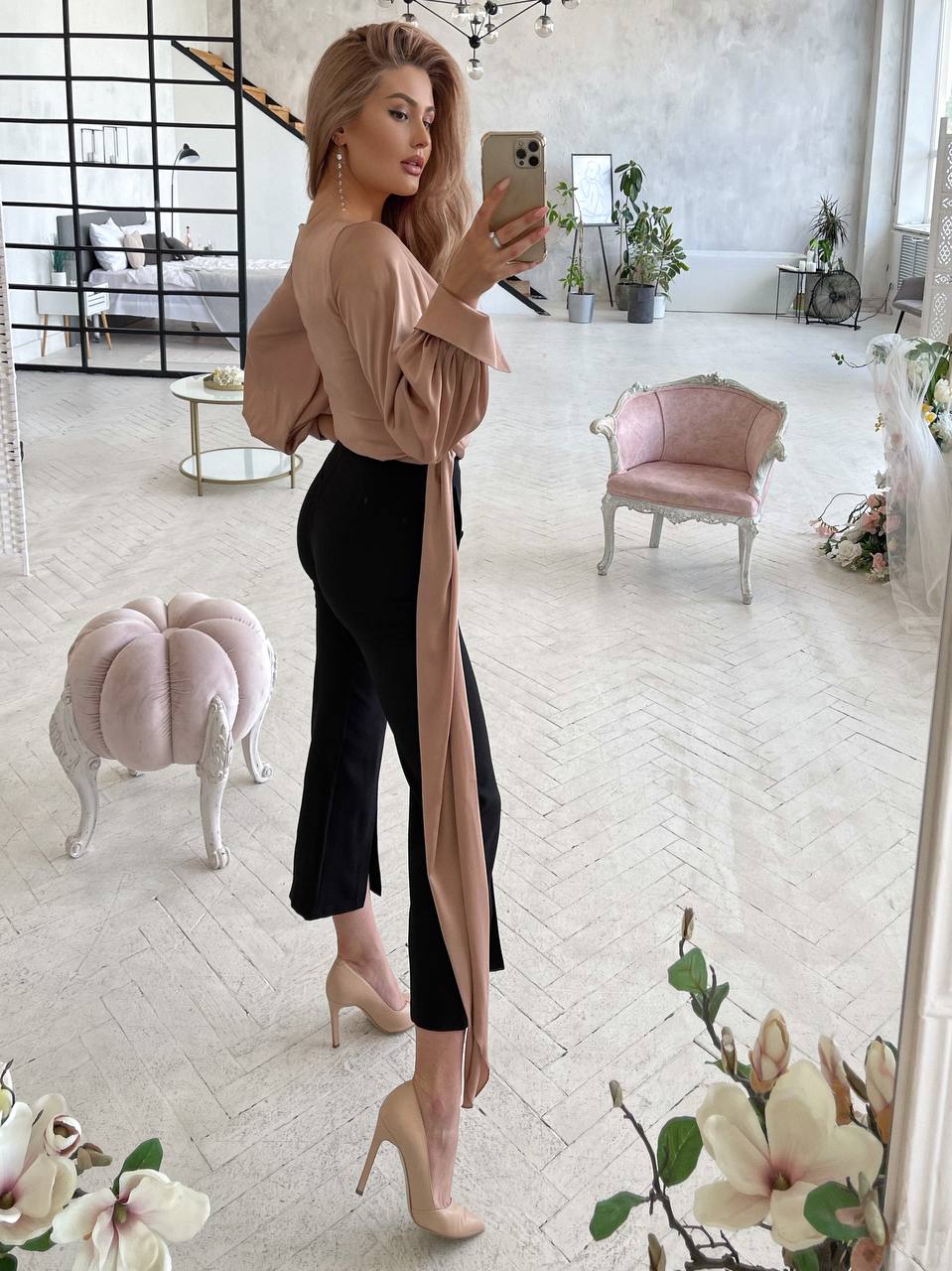 Woman taking a mirror selfie in a stylish outfit with a neutral background