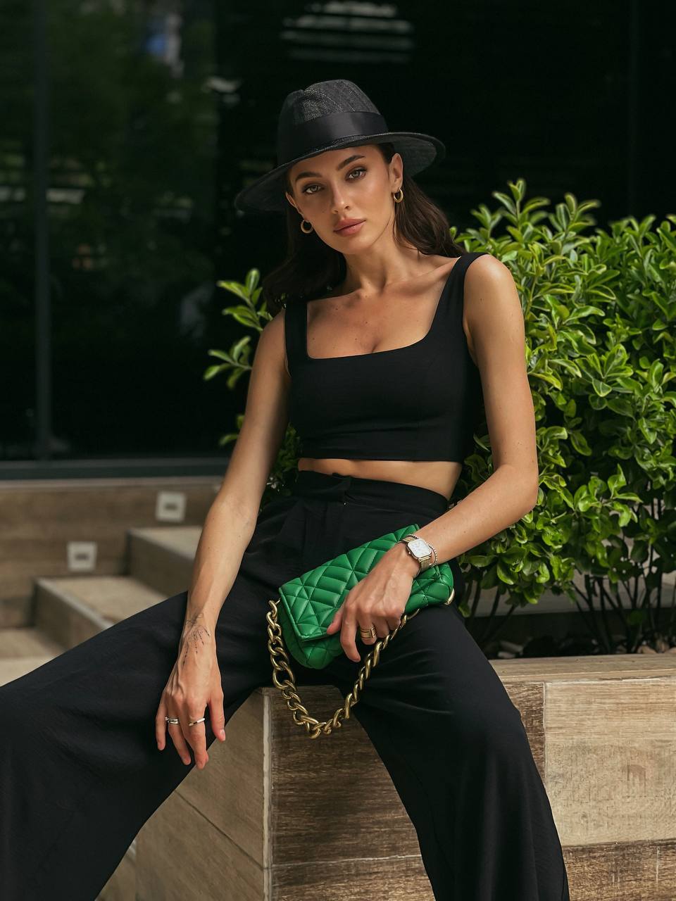 Woman in black outfit with green clutch sitting outdoors