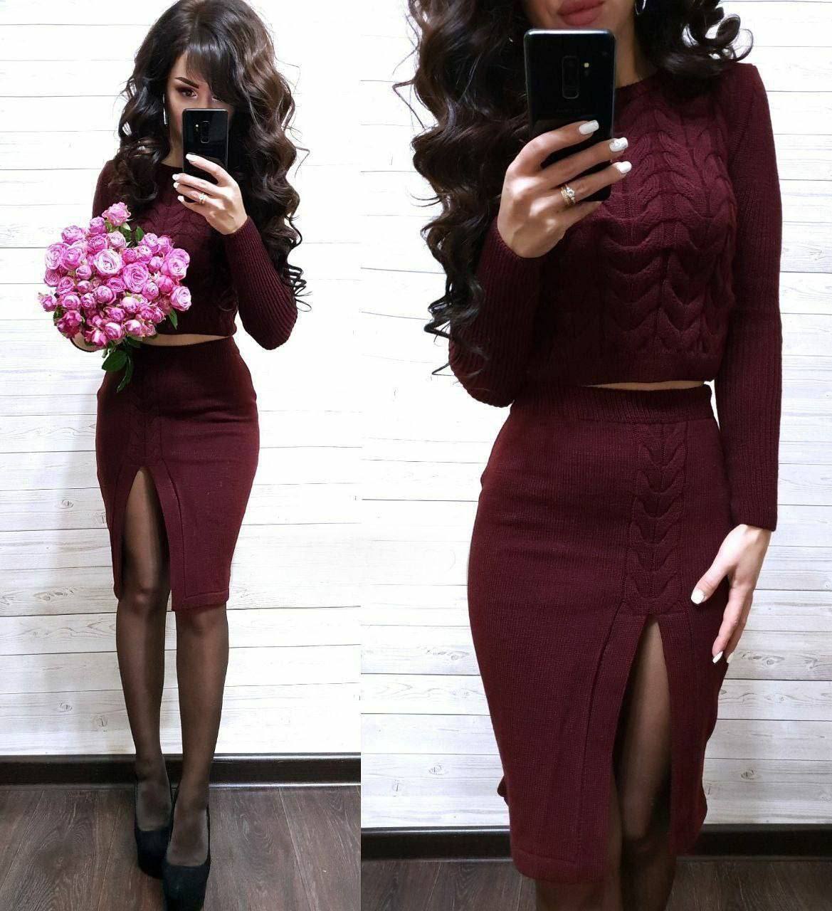 Woman wearing a burgundy outfit with a high slit skirt, holding pink flowers.
