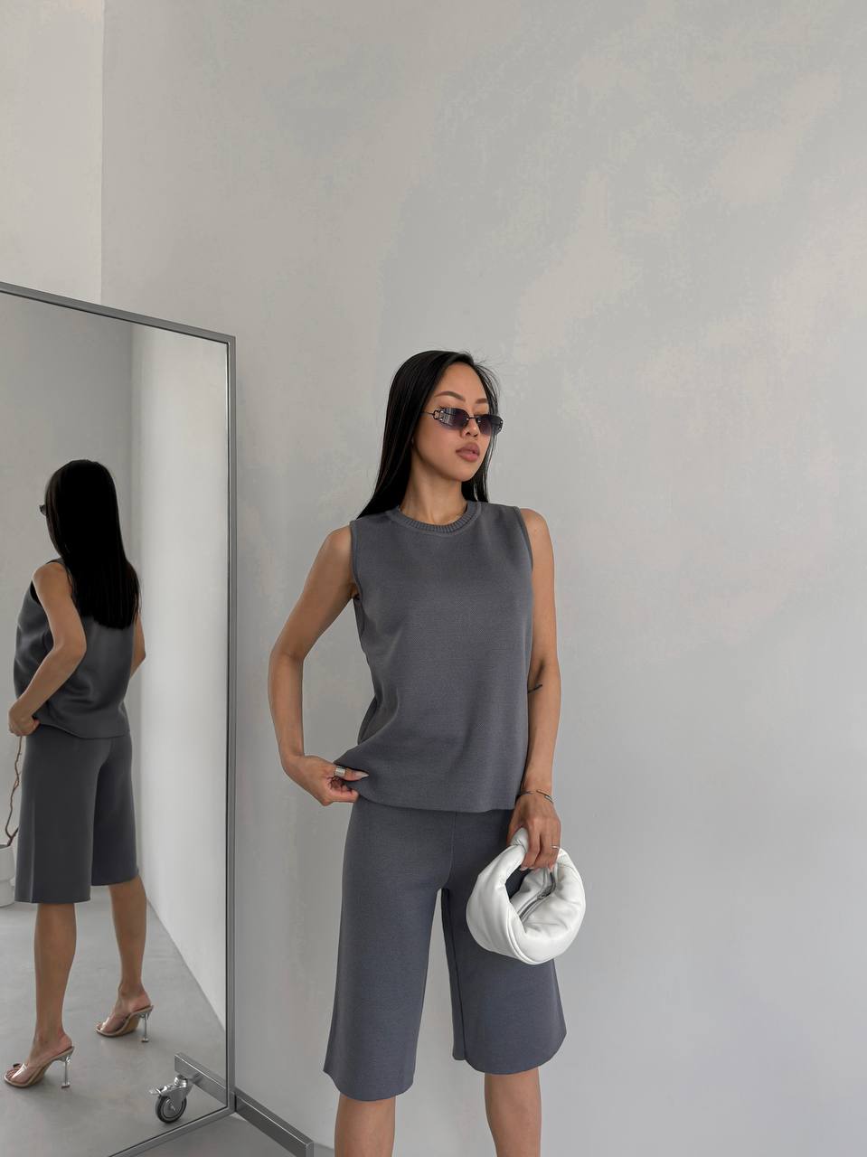 Woman in a gray sleeveless top and shorts standing in front of a mirror.