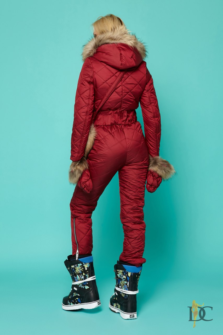 Person wearing a red puffer jumpsuit with fur trim on a teal background