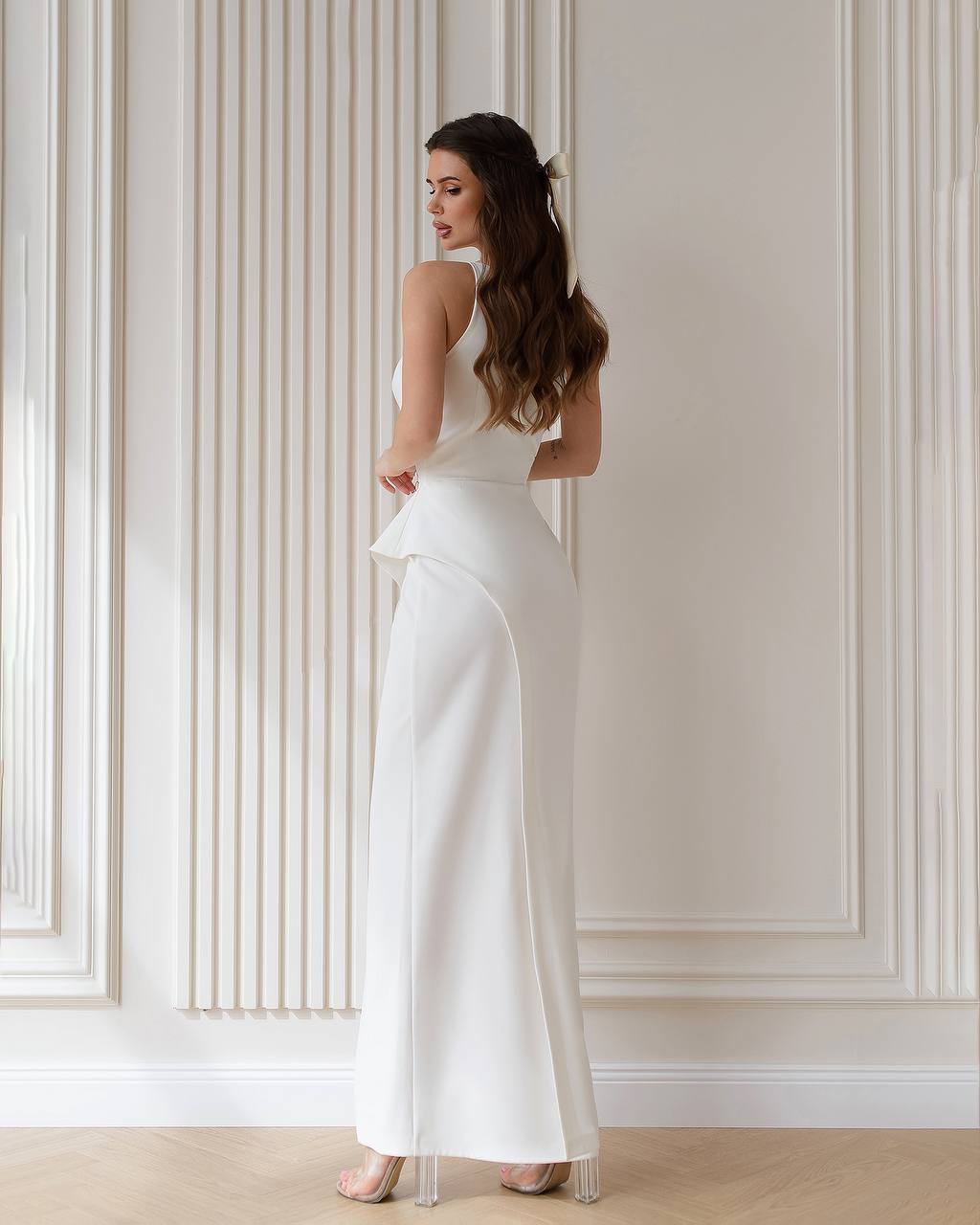 Woman wearing a white sleeveless top and wide-leg pants against a neutral wall.